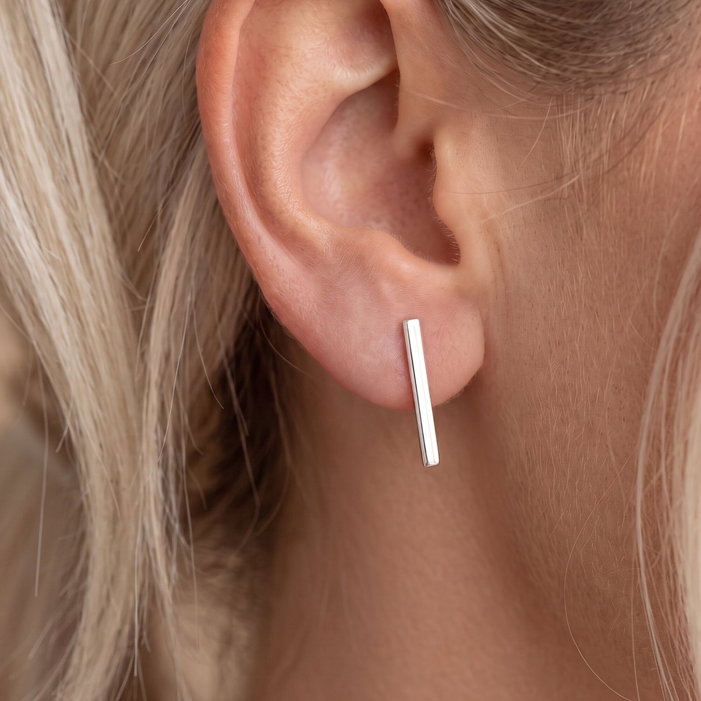 A close-up of a person's ear wearing a minimalist sterling silver bar stud earring.