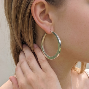 
                  
                    A close-up of a woman wearing a large, polished sterling silver hoop earring on her ear, with her hand resting near her neck.
                  
                