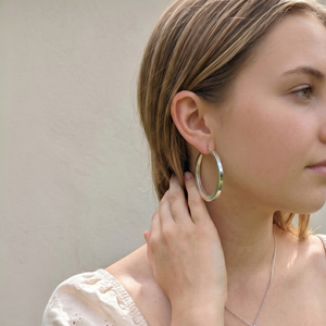 
                  
                    Woman wearing large sterling silver hoop earrings.
                  
                