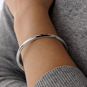 
                  
                    A polished sterling silver bangle bracelet worn on a person's wrist, shown in a close-up shot against a gray knit sweater
                  
                