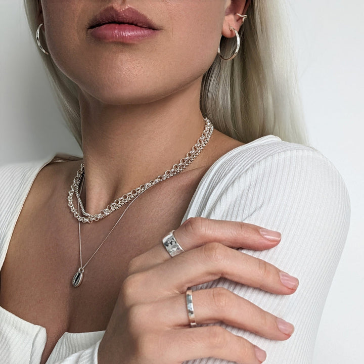 Silver faceted hoops styled with hammered rings, chunky rolo chains and cowrie shell necklace
