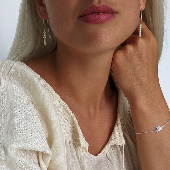 Woman wearing pearl threader earrings and a turtle bracelet, both in sterling silver