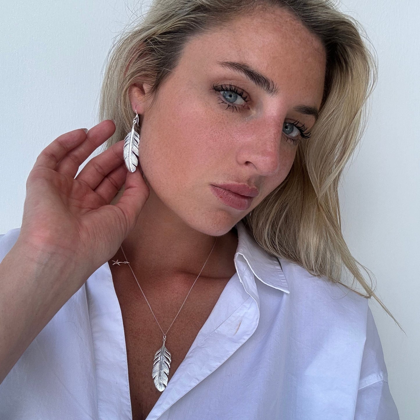 Sterling silver feather pendant necklace styled with matching feather earrings — nature-inspired set