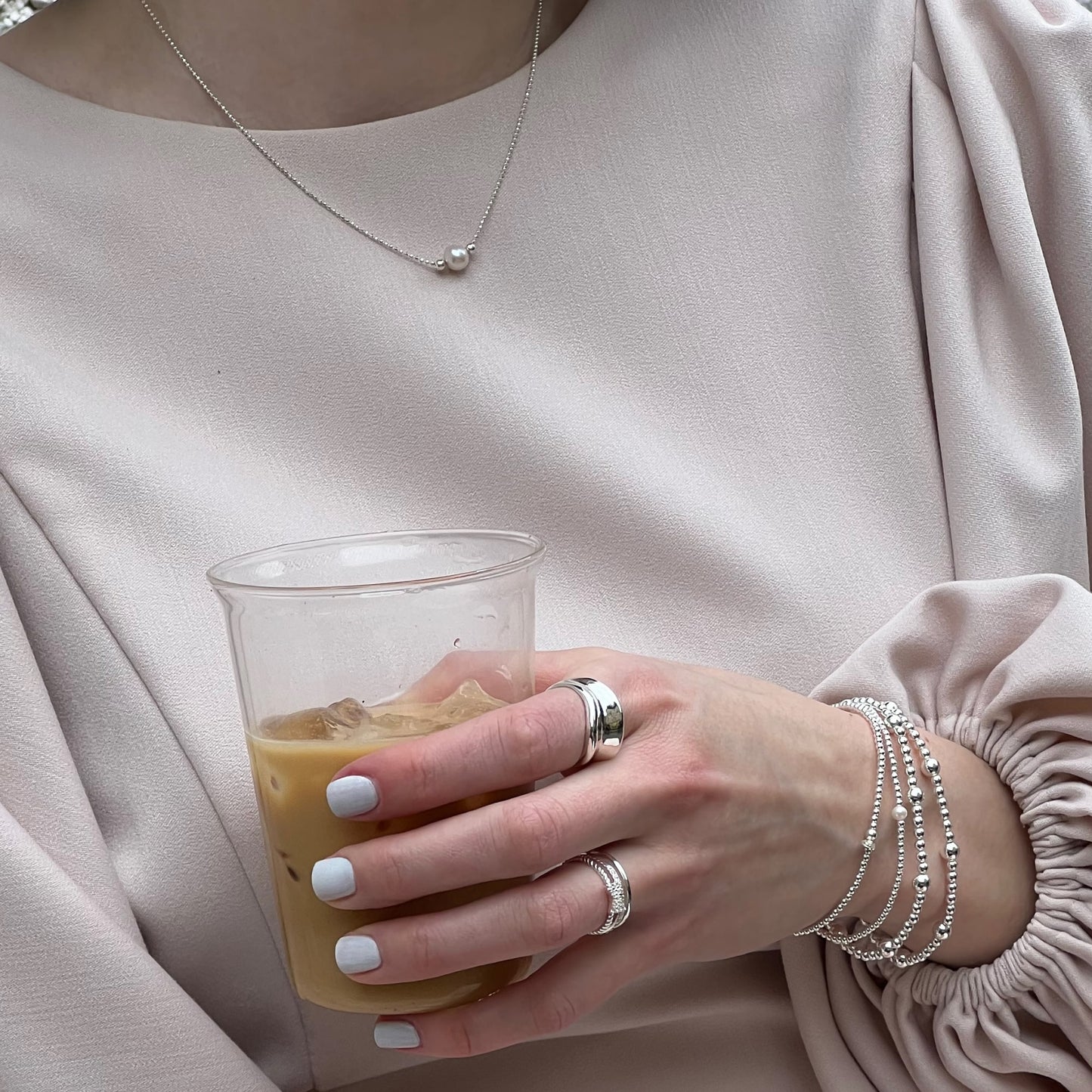 Chunky sterling silver concave ring worn with cubic zirconia rings, a pearl necklace, and beaded bracelets