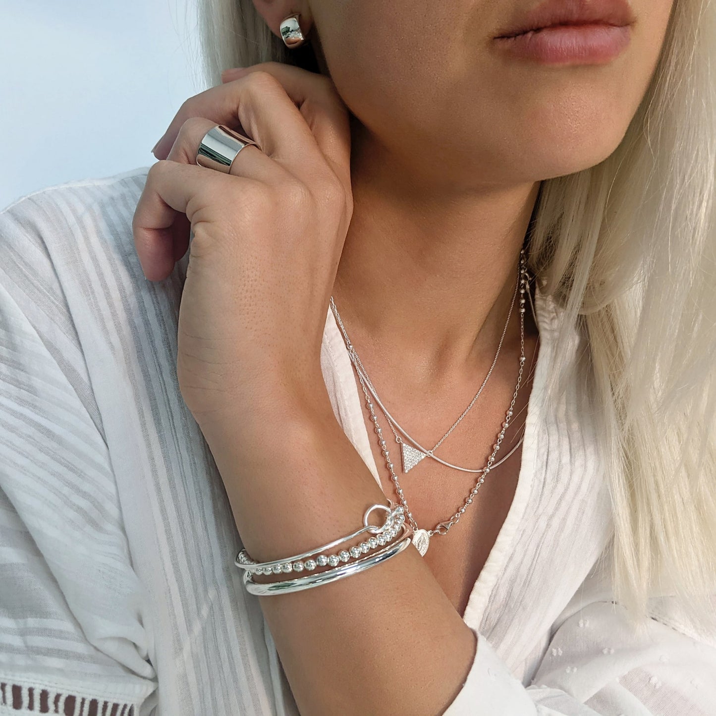 Silver friendship bracelet styled with chunky huggie earrings, a ball bracelet, and a wide band ring