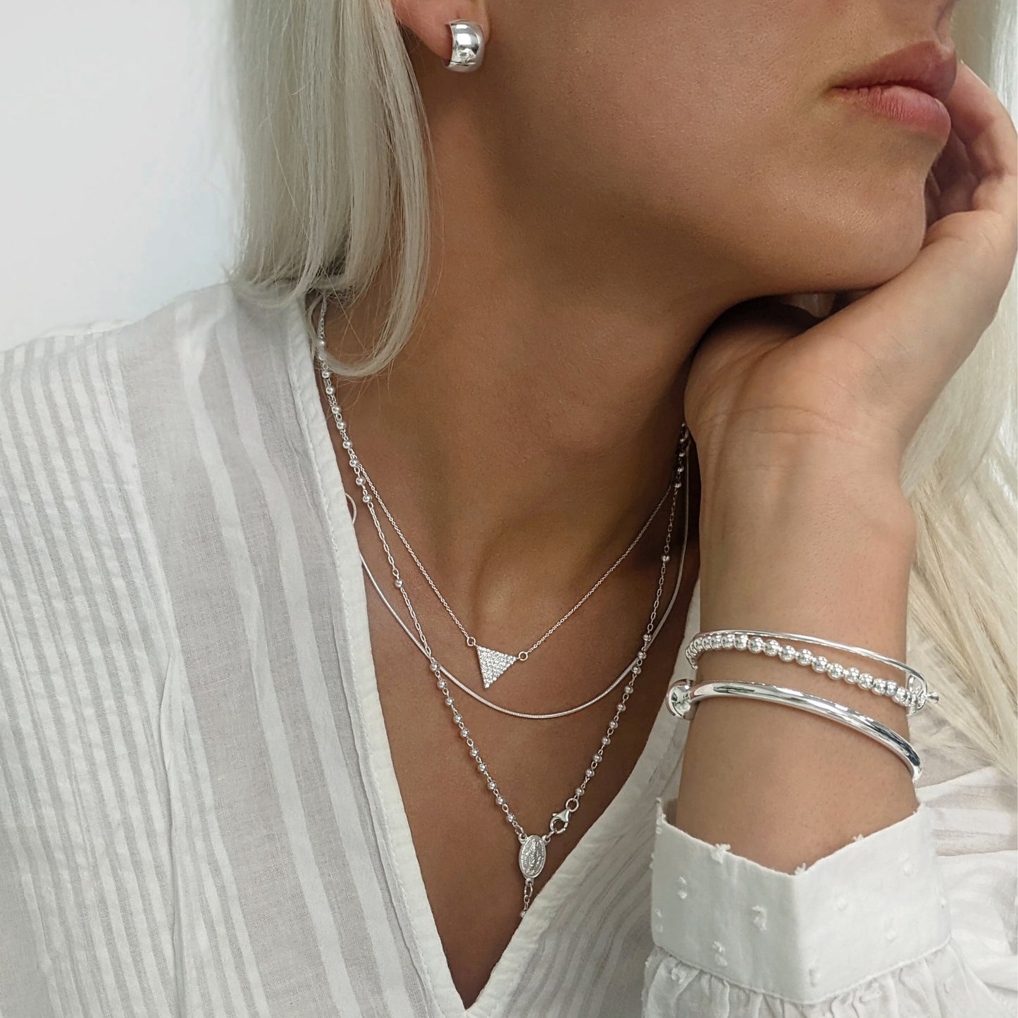 Dome huggies styled with knot bangle, ball bracelet, rosary necklace and CZ triangle pendant, all in sterling silver