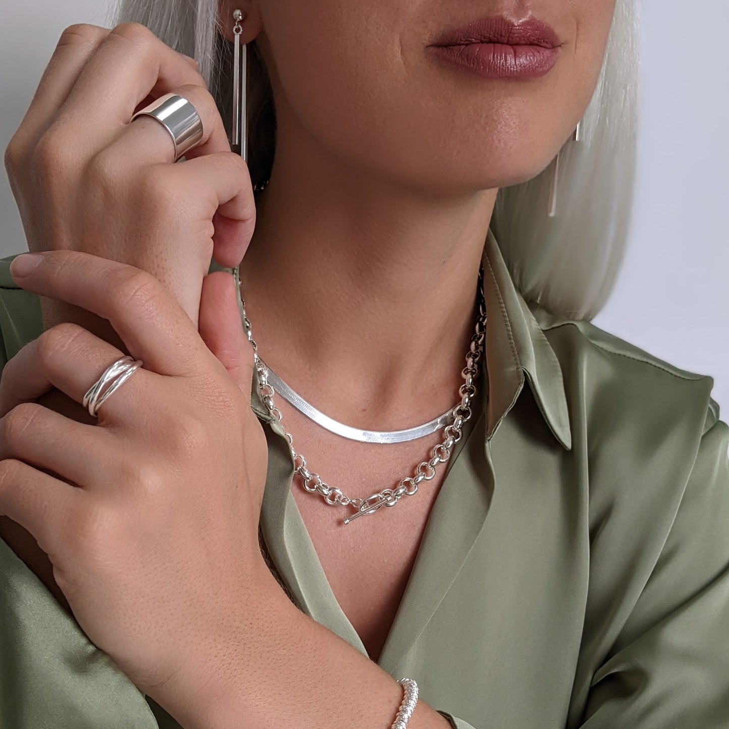 Sterling silver jewellery look — layered herringbone chain and chunky rolo chain, styled with chunky band ring, wrap ring and long bar drop earrings