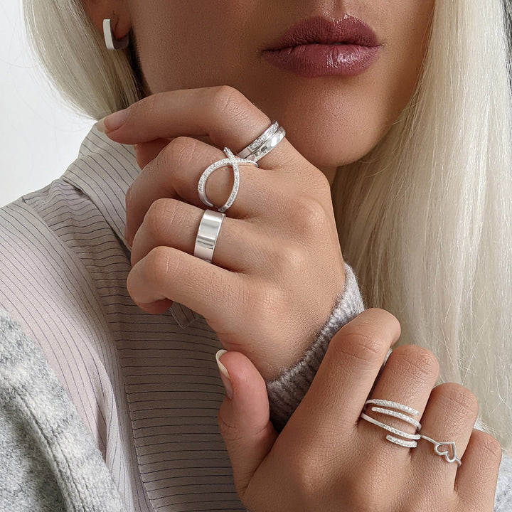 Sterling silver rings styled together — hammered band, crossover pavé ring and chunky band on one hand; multi-row pavé ring and heart ring on the other