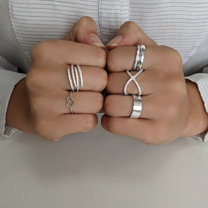 Sterling silver ring stack — multi-row pavé ring and heart ring on one hand, hammered band, crossover pavé ring and chunky band on the other