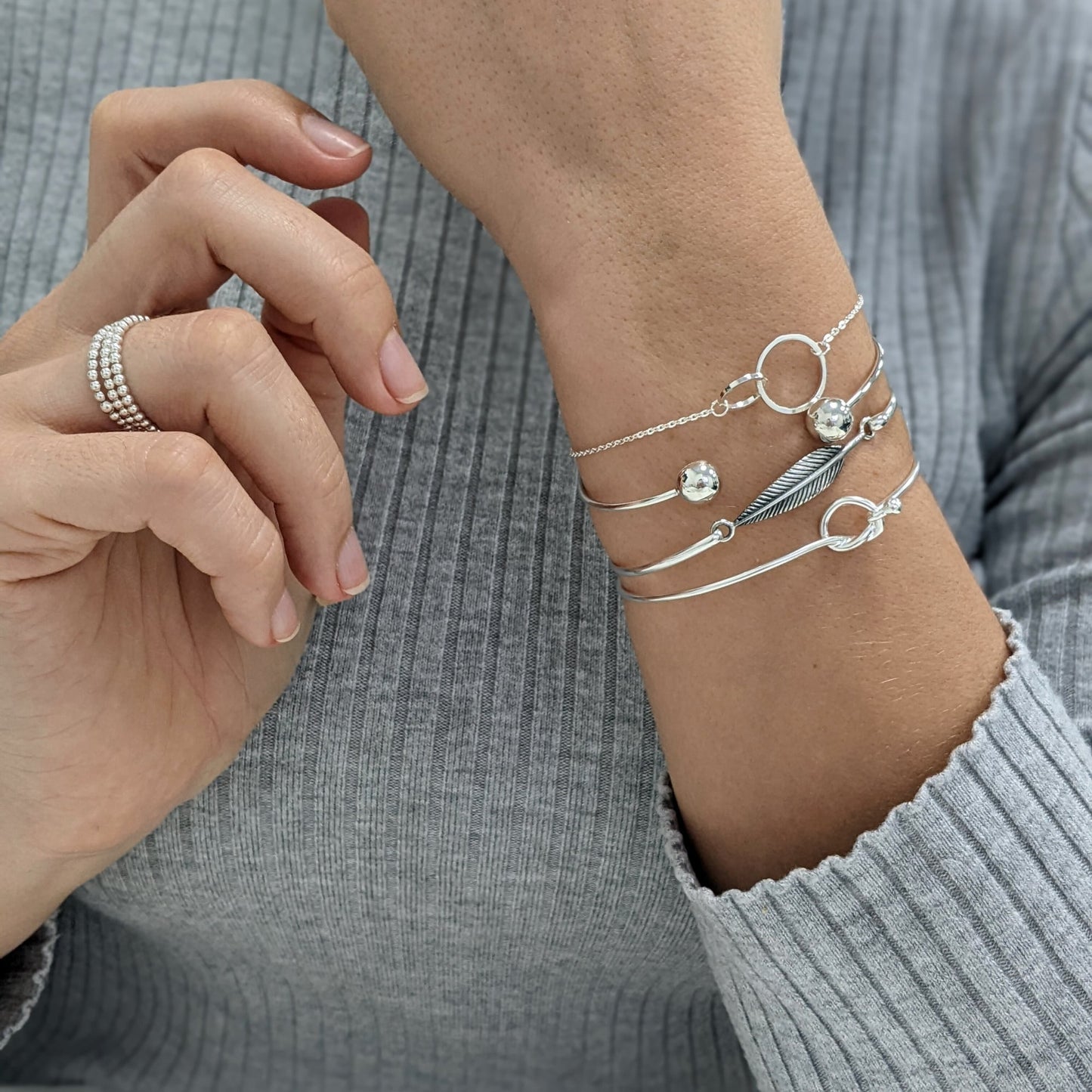925 silver knot bangle paired with a feather bangle and a linked circle chain bracelet