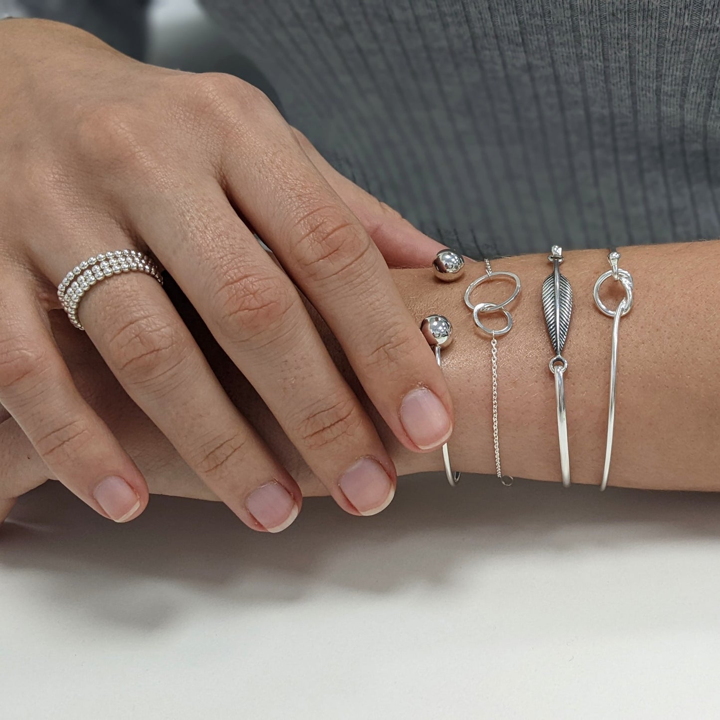 Sterling silver friendship knot bracelet styled with a feather bangle and beaded rings — boho jewellery look