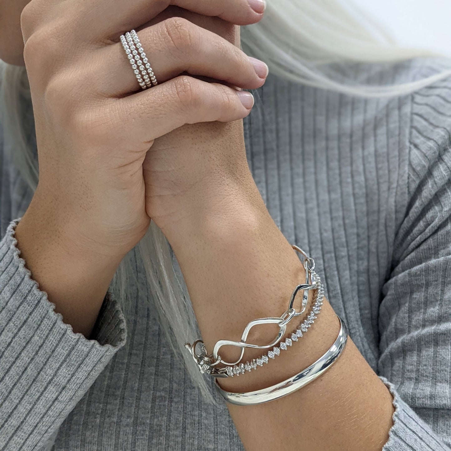 Model wearing three stacked beaded rings, an infinity link bracelet, a CZ tennis bracelet, and a D-shape bangle, all in 925 silver
