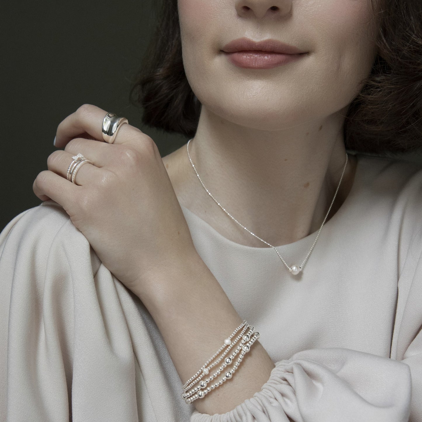 Sterling silver jewellery look — pearl pendant necklace styled with chunky band ring, CZ band rings, and layered beaded bracelets