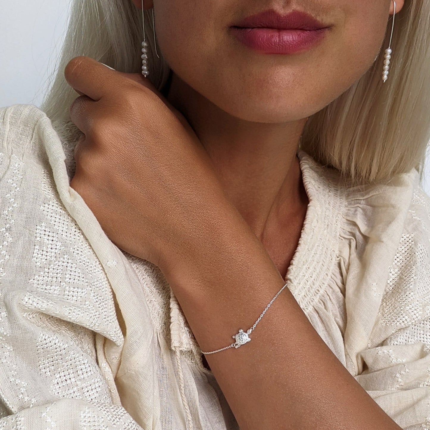 Woman wearing long pearl bead earrings and a turtle bracelet, both in sterling silver