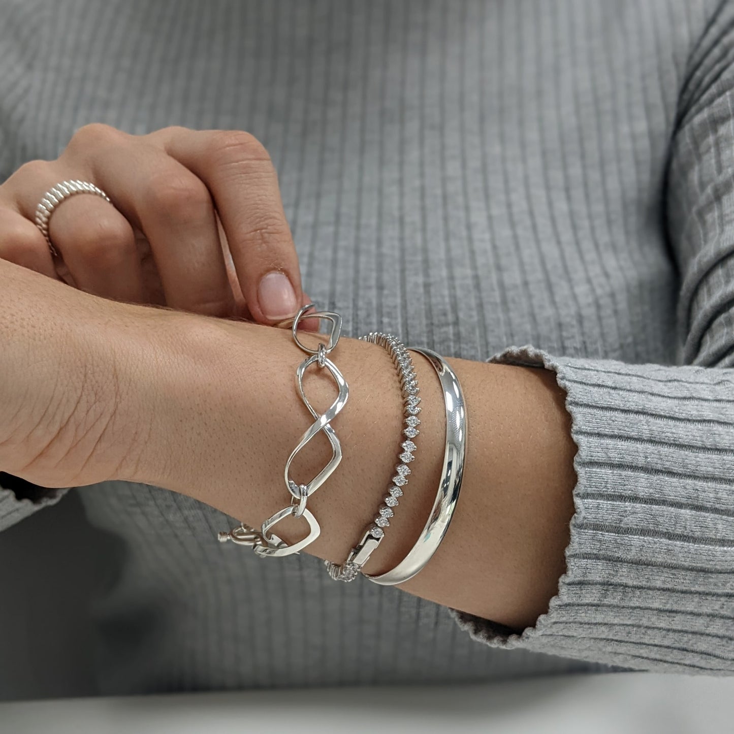 Woman wearing infinity link bracelet, tennis bracelet, and D-shape bangle, all in 925 silver