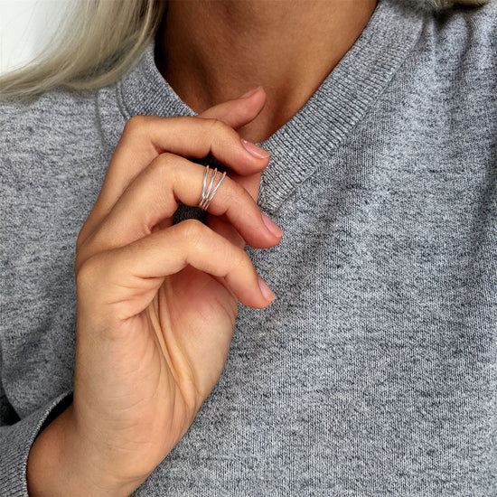 
                    
                      Sterling silver triple band midi ring worn on the upper finger of a woman's hand resting near her collar.
                    
                  