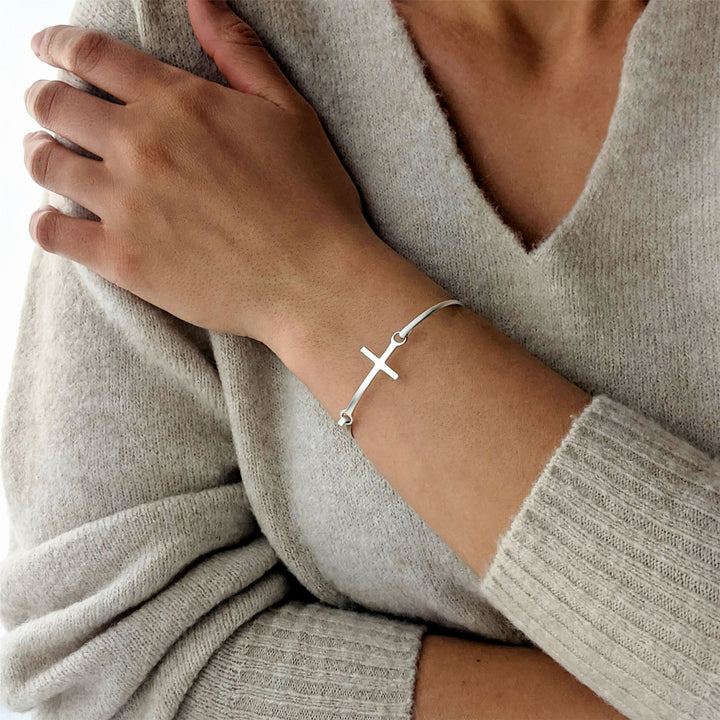 Woman wearing sterling silver sideways cross bangle with hook clasp.