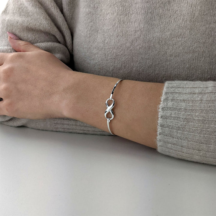 925 sterling silver infinity symbol bangle worn on the wrist, featuring a polished figure-of-eight infinity charm on a slim bangle band