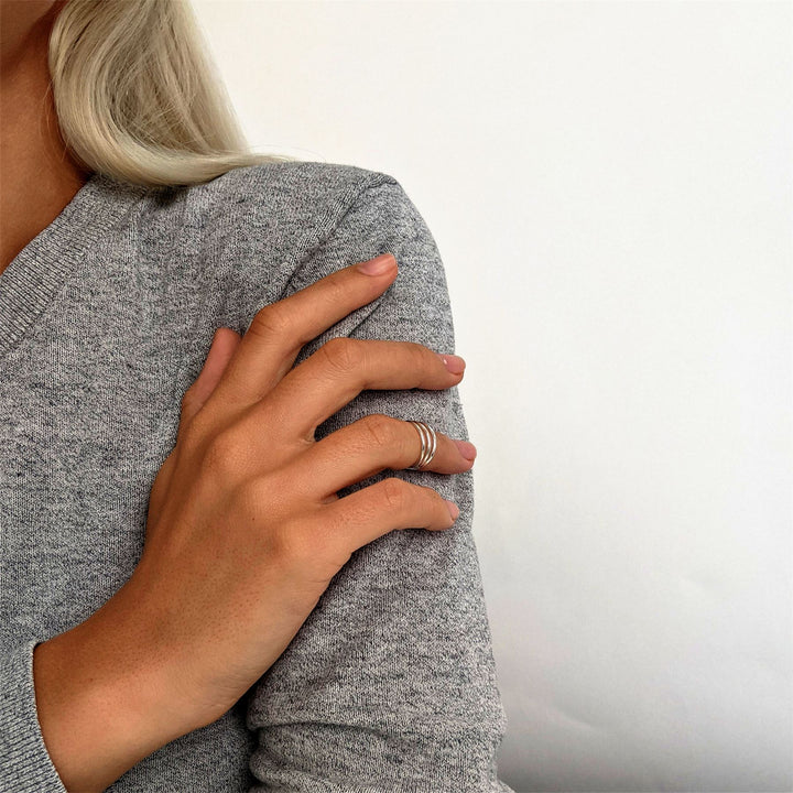 Sterling silver triple band midi ring worn on the upper finger of a woman's hand resting on her shoulder.
